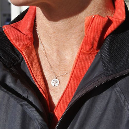 Sterling silver tree charm necklace worn outdoors with red jacket