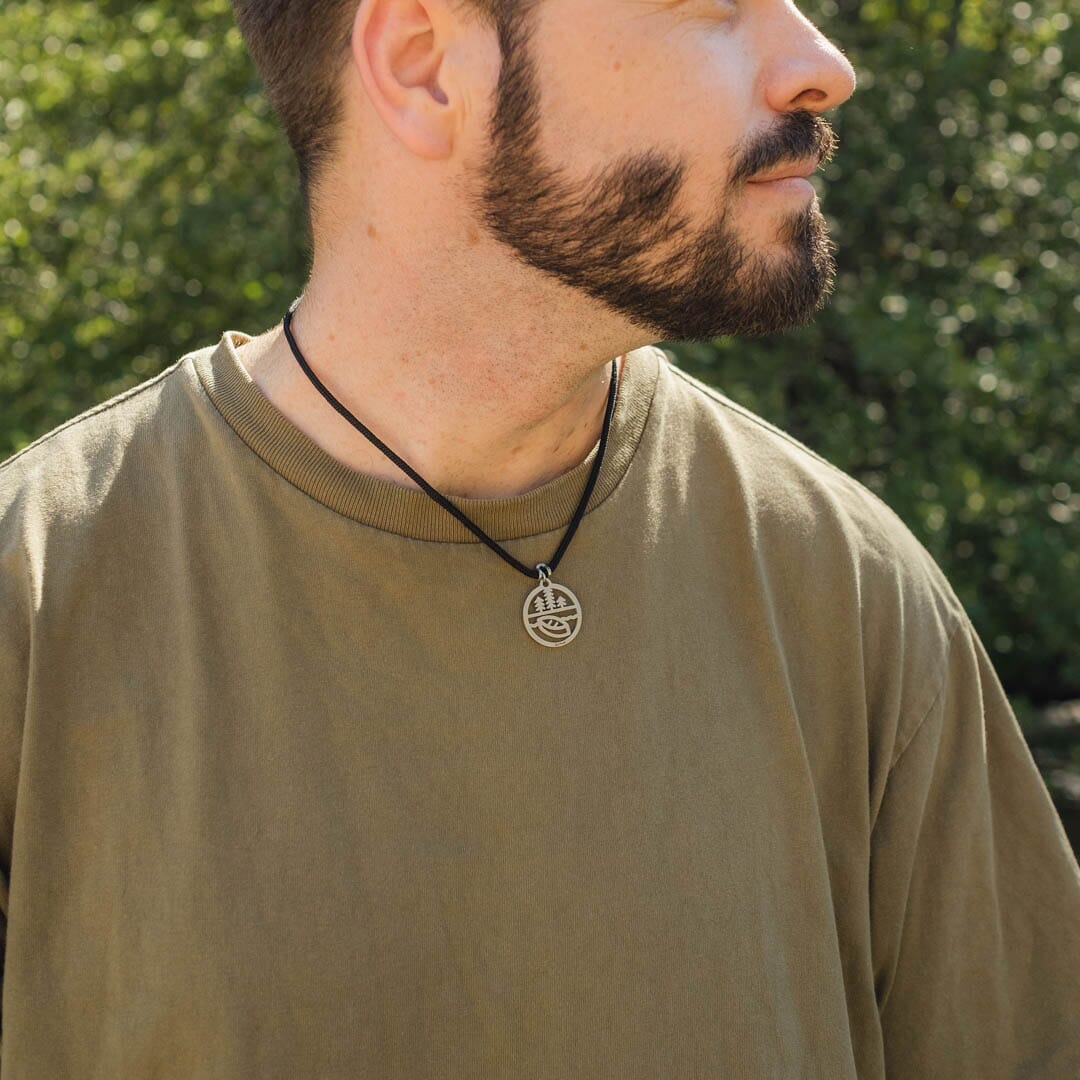 Man wearing stainless steel canoe and trees pendant on black paracord