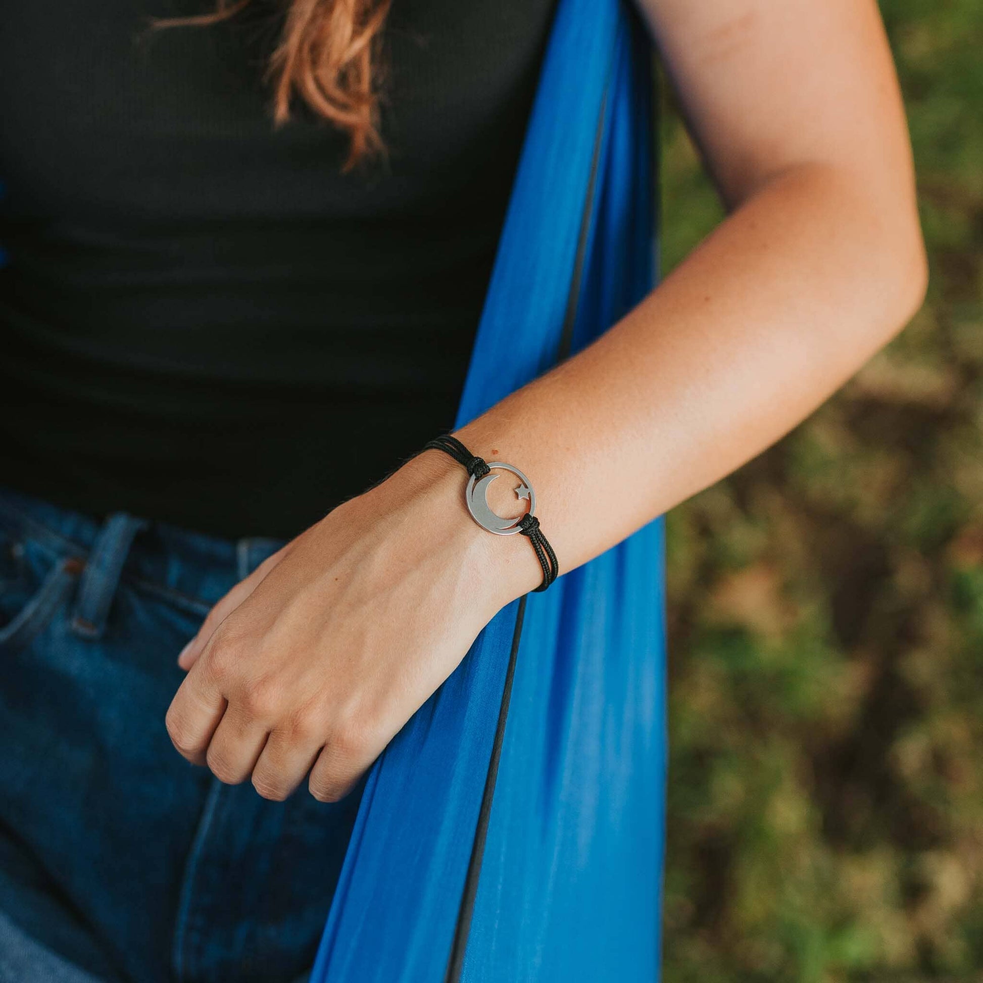 Girl hammocking wearing stainless steel moon and star bracelet on black paracord